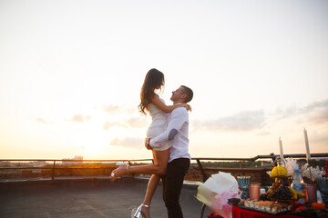 Couple celebrates romantic sunset on rooftop with elegant table setting and joyful embrace