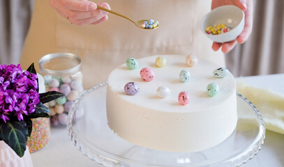 cropped shot of young woman making Easter cake in pastel colors in the kitchen, decorating with sprinkles