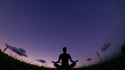 Peaceful figure sits in meditation, silhouetted against a vibrant sunset sky. Soft colors transition as the evening descends, creating a calming ambiance