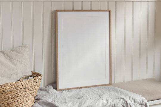 Empty vertical portrait A2 thin wooden frame mockups with linen cloth on bench. White beadboard wainscot wall paneling background. Straw French basket, linen pillow cushion. Scandinavian interior home
