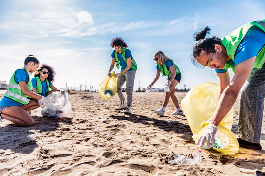 Group of eco volunteers picking up plastic trash on the beach - Activist people collecting garbage protecting the planet - Ocean pollution, environmental conservation and ecology concept.