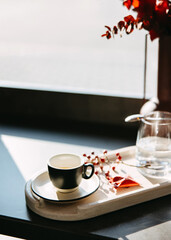 Minimalist coffee moment with an espresso on a wooden tray, in warm morning sunlight.