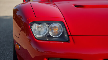Fototapeta premium Close-up view of a sleek red sports car showcasing its modern headlight design during golden hour in an outdoor setting
