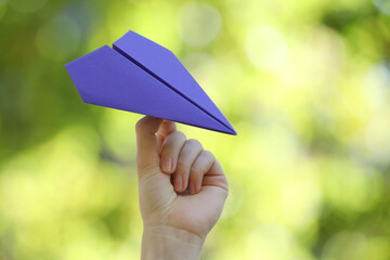 Woman with handmade paper plane on blurred green background, closeup
