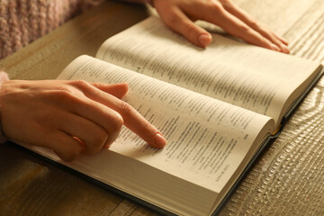 Woman reading Holy Bible at wooden table, closeup
