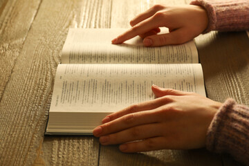 Woman reading Holy Bible in English language at wooden table, closeup