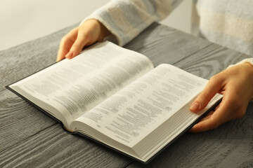 Woman with open Holy Bible in English language at wooden table, closeup