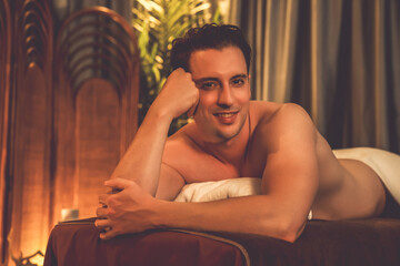 Obraz premium Caucasian man customer enjoying relaxing anti-stress spa massage and pampering with beauty skin recreation leisure in warm candle lighting ambient salon spa at luxury resort or hotel. Quiescent