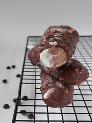 Chocolate-coated ice cream bars with nuts are displayed on a cooling rack, surrounded by scattered chocolate chips.