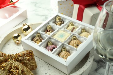 Box with tasty sweets in shape of baubles, wine and Christmas decor on white marble background, closeup