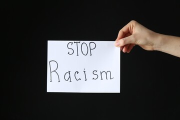 Woman holding card with phrase Stop Racism on black background, closeup
