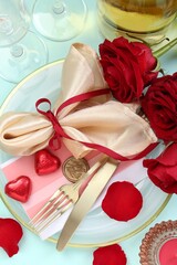Romantic place setting with cutlery, hearts and red roses on light blue background, flat lay. Valentine's day celebration