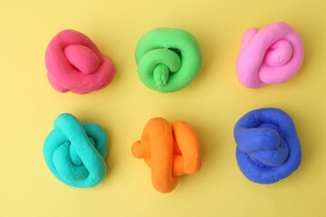 Different colorful play dough on yellow background, flat lay