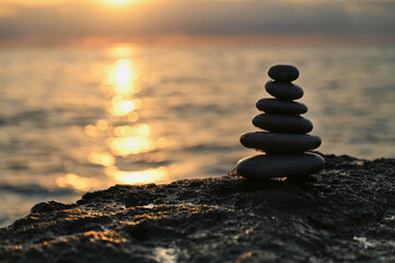 A careful arrangement of smooth, dark stones sits atop a rocky surface, glistening in the sunlight reflecting off calm ocean waters during a serene sunset.