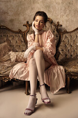 Obraz premium A beautiful young woman dressed as a nymph relaxes on an ornate vintage couch, exuding charm.