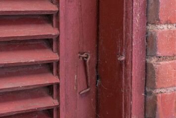 Closeup, red door and hook with lock for old exterior, damage or vintage doorframe of abandoned home. Empty, entrance or weathered wood with poor safety or scuff marks for security construction