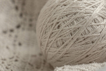 A ball of beige knitting yarn lies on a crocheted fabric macro