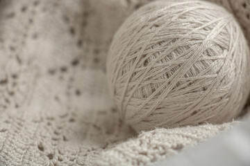 A ball of beige knitting yarn lies on a crocheted fabric