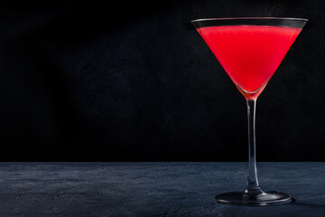 Cosmopolitan cocktail with vodka and cranberry juice in an elegant glass, on a black background