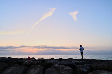 In the early morning light, a lone fisherman stands on a rocky shoreline, casting his line into the...