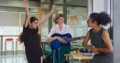 Indian Asian happy young adult gen z girl hold guitar play music make fun joy job office place crazy boss lady teen female multi staff group team do funny dance sing song spend time enjoy work break