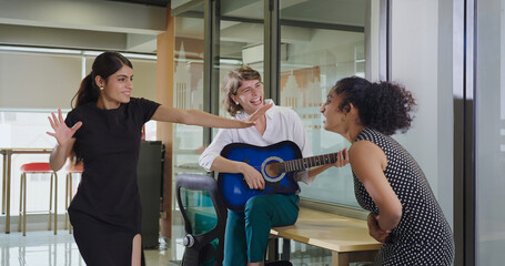 Indian Asian happy young adult gen z girl hold guitar play music make fun joy job office place crazy boss lady teen female multi staff group team do funny dance sing song spend time enjoy work break