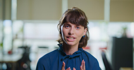 Happy gen z woman lady intern sitting look cam do work casual talk client on video call day office. Head shot young adult worker expert female girl speak casual share idea plan teach study job place