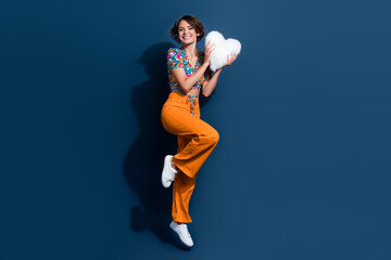 Full length photo of lovely young lady hold white fluffy heart pillow dressed stylish flared pants isolated on dark blue color background