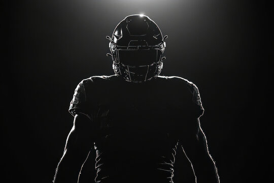 An American football player in uniform and helmet, silhouetted on a black background