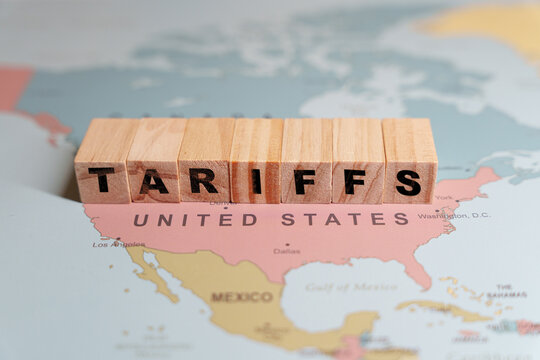 Wooden blocks spelling TARIFFS are placed on a map of North America, specifically over the United States and Mexico