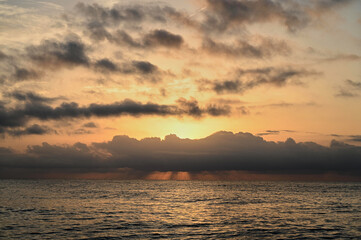As the sun dips below the horizon, golden hues spread across the sky, illuminating clouds with deep shades of orange and pink. The ocean reflects the beauty in tranquility, inviting moments of peace.