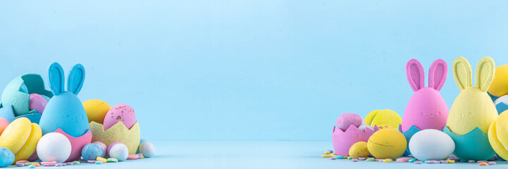 Cute and bright pastel colored Easter eggs and bunny background. Pink. blue, yellow colored bunny rabbits, chocolate eggs in nests and eggshell baskets, sugar sprinkles on light blue background