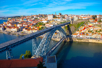 Obraz premium The Dom Luis I Bridge spans the Douro River in Porto, Portugal, connecting historic cityscape with Vila Nova de Gaia. Stunning blend of iron architecture and colorful riverside houses under a blue sky