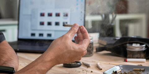 Asian male creative industries worker, smoking cannabis buds in an office, surrounded by a relaxed...