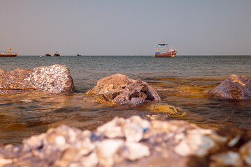 Infrared photography, a calm ocean scene with a focus on rocks in the foreground, a few boats on the horizon