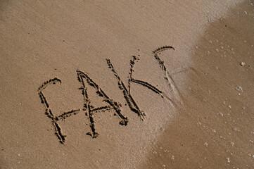 On a tranquil beach, bold letters spelling out FAKE are etched into the warm, golden sand. Gentle waves lap at the shore, blurring the edges of the message as the tide shifts.