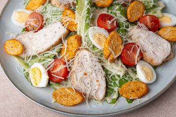 Caesar salad with chicken, cherry tomatoes, croutons, parmesan cheese, quail eggs and romaine lettuce. Traditional American dish. Close-up, selective focus.