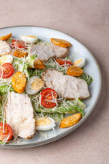 Caesar salad with chicken, cherry tomatoes, croutons, parmesan cheese, quail eggs and romaine lettuce. Traditional American dish. Close-up, selective focus.