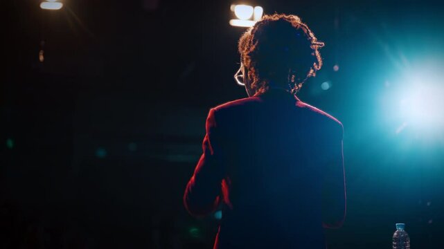 Back view of male comedian on stage, man speaking jokes and funny stories. Entertainment and leisure, professional artist speaking comical monologues or singing songs, performance in nightclubs
