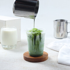 Iced matcha milk, A vibrant green tea beverage is being poured freshly into a cup, surrounded by milk and elegant cafe tools in a minimalist environment