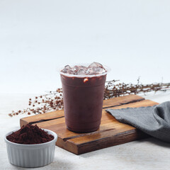 Iced chocolate, A chilled beverage filled with ice sits alongside a bowl of cocoa powder on a wooden surface, creating a tempting snack moment