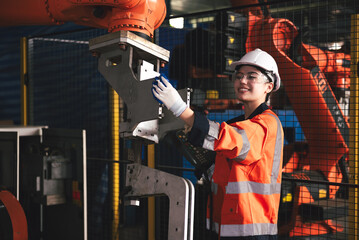 Beautiful female engineer wearing a hard hat and safety gear while overseeing robotic arm...
