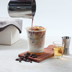 Rich coffee poured over ice and cream in a layered glass, set on a wooden board with another glass and coffee beans nearby