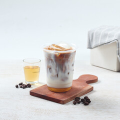 Iced coffee with milk sits on a wooden board alongside coffee beans and a glass of cool water in a minimalistic setting