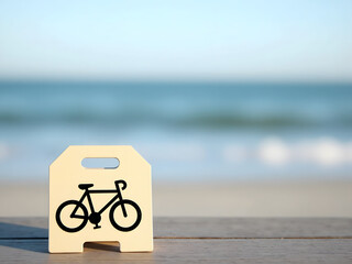 A bike-shaped sign stands on a wooden surface with a blurred beach and ocean background creating a calm, inviting scene