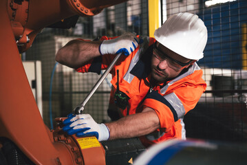 Caucasian engineer maintaining an automatic robotic arm in a smart factory, showcasing industrial automation, technology, and innovation in modern manufacturing.