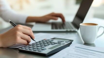 Fototapeta premium Taxes and government advice, A person calculates finances using a calculator while working on a laptop, surrounded by paperwork and a coffee cup.