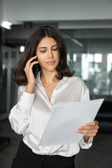Middle aged latin businesswoman having business phone call with partners, clients, looking at...