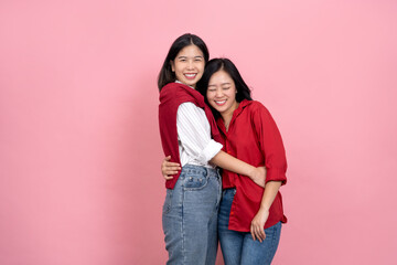 Two Asian girls with long hair in red and white shirts are posing as a LGBTQ couple on a pink background.