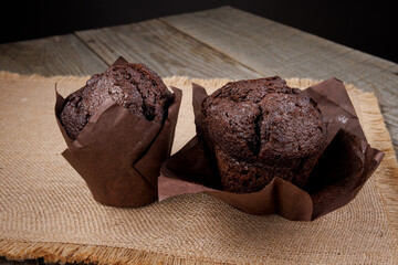 Two chocolate muffins in a paper cup on a burlap napkin.